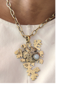 Gold necklace with a detailed pendant on a person wearing a white shirt.