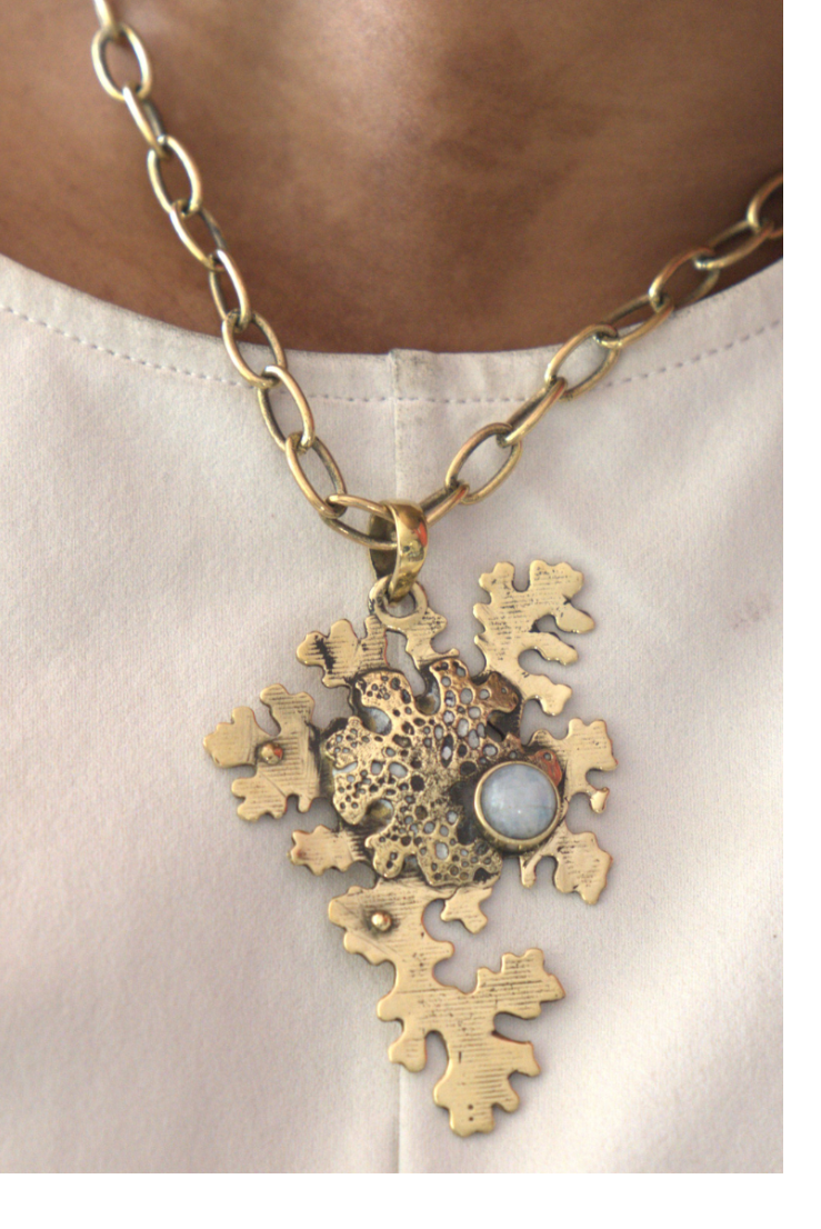 Gold necklace with a detailed pendant on a person wearing a white shirt.